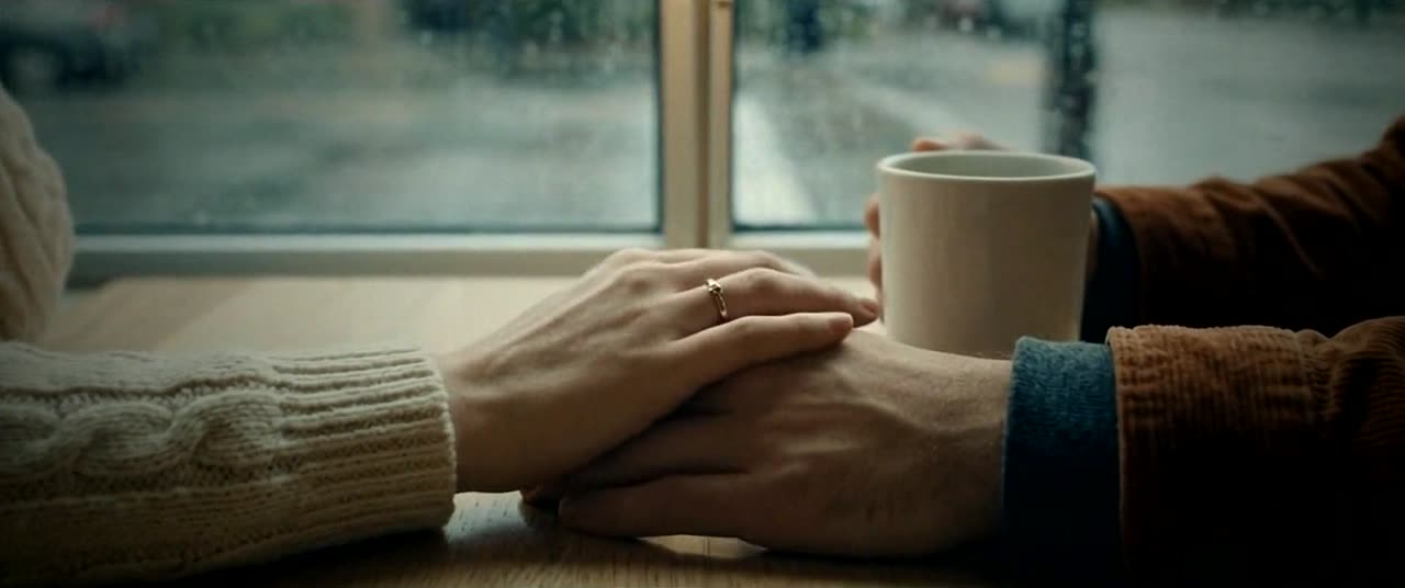 Maya’s hand covers Eli’s on the cafe table beside a mug