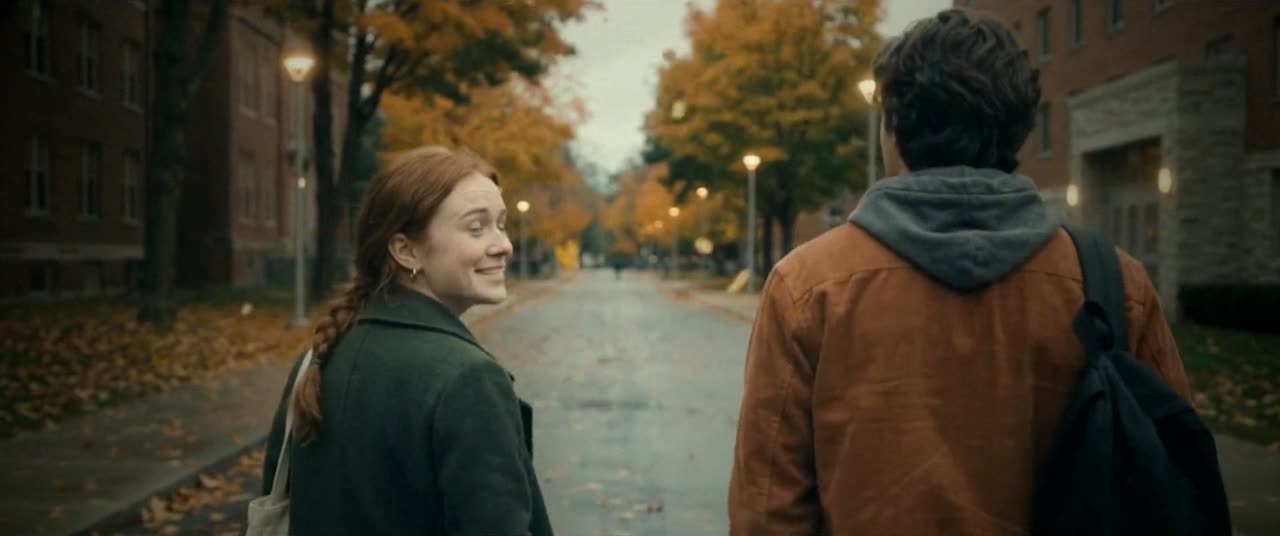 On an autumn street, Maya turns back to Eli with a smile